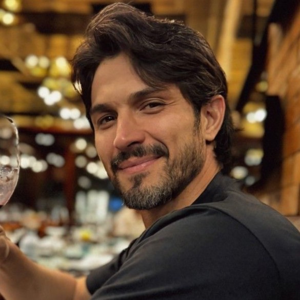Retrato de um homem de cabelos escuros e barba sorrindo.