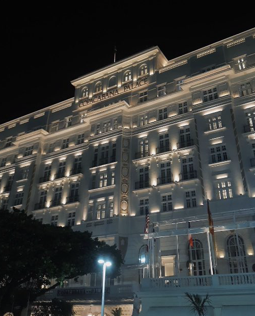 Fachada iluminada de um edifício à noite, com o letreiro COPACABANA PALACE.