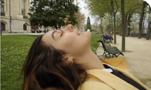 Isabela Alencar recostada em um banco de parque, de olhos fechados.