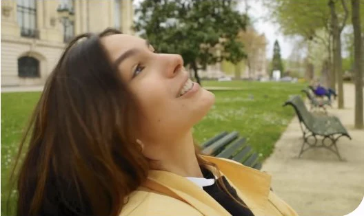 Isabela Alencar sorrindo enquanto se recosta em um banco de parque.